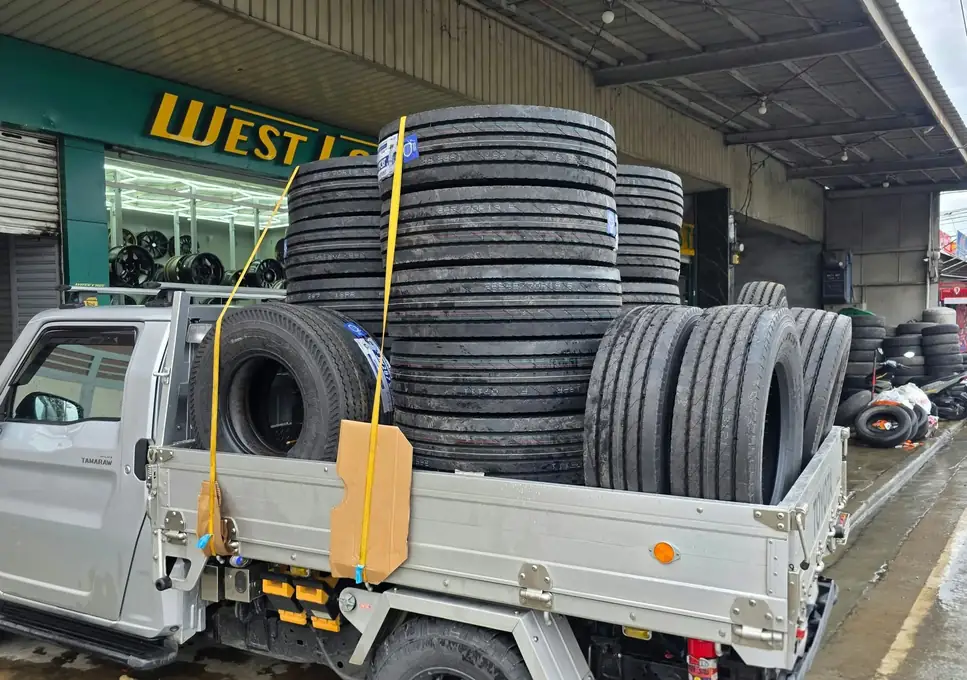 Truck tires stacked high on a small truck in front of the shop